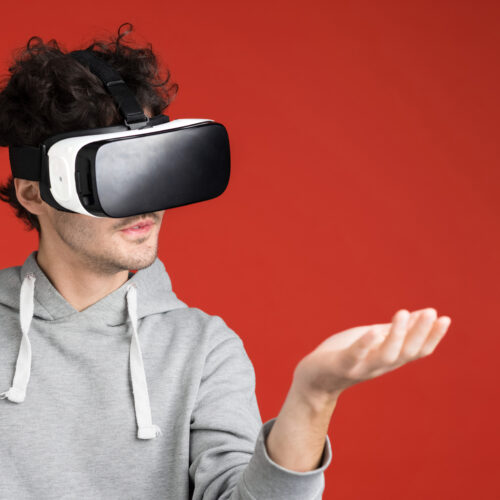 A young man is playing games using VR glasses, holding a virtual thing, red background